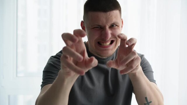 Young brunette man in a bright room making playful hand gestures as if flirting or jokingly trying to attract someone&rsquo;s attention. Concept of lighthearted interaction and social confidence