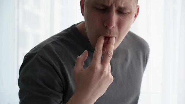Young brunette man in a bright room putting two fingers in his mouth to whistle loudly, trying to attract attention. Concept of calling, signal, and getting noticed.