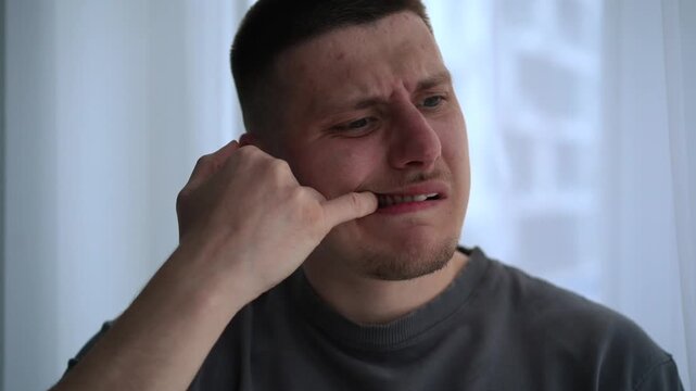 Close-up of a young man opening his mouth and checking between his teeth with his fingers in a bright room. His calm but slightly uneasy expression suggests minor irritation rather than pain.