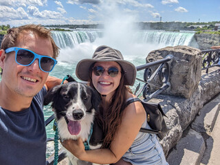 Obraz premium A young couple and their dog smile for a selfie with Niagara Falls in the background during a sunny day in the summer.