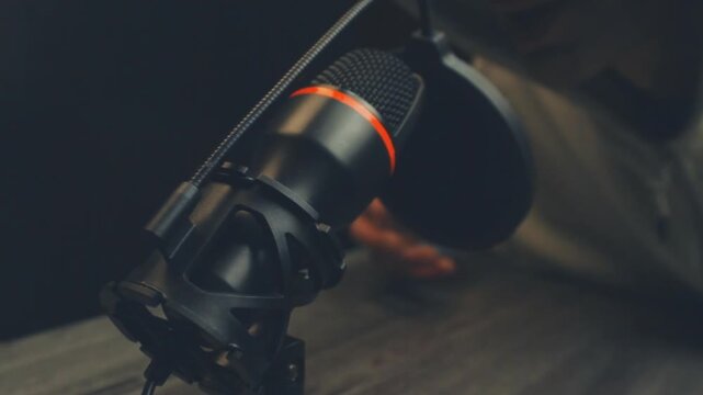 Close up of a black studio microphone while a blurred person speaks and gestures in the background recording a podcast or vlog