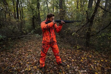 Naklejka premium Hunter in Orange Gear Aims Shotgun in Forest During Autumn