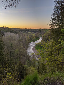 A high angle view of a beautiful creek in a forest valley at sunset. Trees begin to bud in this landscape shot during the spring with a highway bridge in the distance.