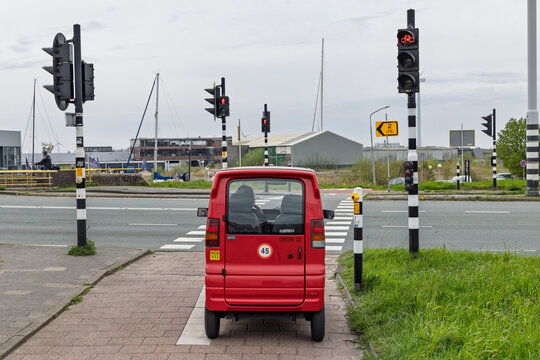 Amsterdam, Netherlands, April 11, 2026. A red Dutch Canta LX microcar for disabled drivers stopped at a red traffic light on a bike path crossing.