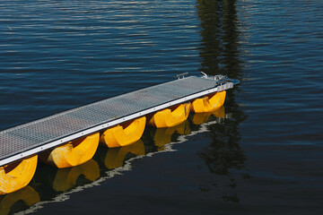 Floating dock with yellow plastic pontoons on calm blue water © Elninho