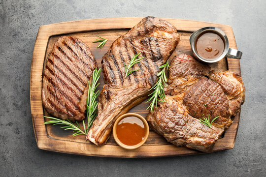 Grilled beef steaks with sauce and rosemary on grey table, top view
