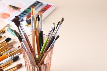 Obraz premium Paintbrushes in glass and paints on beige background, closeup. Space for text
