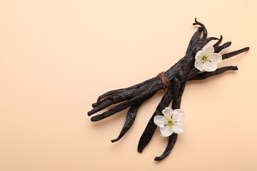 Fototapeta premium Vanilla pods and flowers on beige background, top view. Space for text