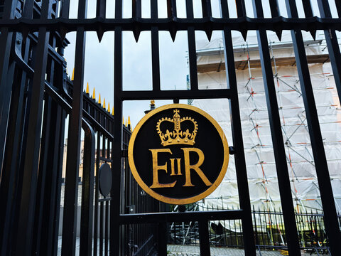 Black iron gate with gold EIIR royal emblem at a London, UK historic entrance with scaffolding and restoration