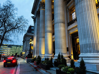 Naklejka premium Illuminated classical Four Seasons Hotel London at Ten Trinity Square building with tall columns on a London, UK street at dusk