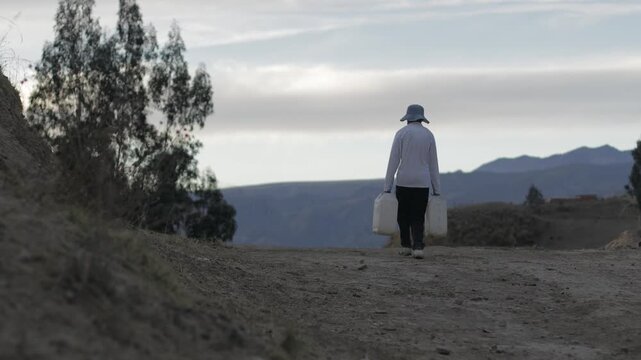A young man, struggling to carry two full jerrycans across the mountains, seen on the horizon