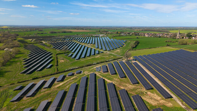 Aerial view of a large solar farm with rows of photovoltaic panels across green fields under a blue sky near Nailstone, England, United Kingdom.
