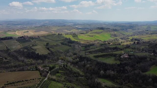 Wide landscape panorama with patchwork fields, wooded valleys, and distant hills under a cloudy spring sky.