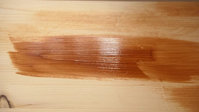 Hand brushing dark stain across wooden board during indoor renovation work.