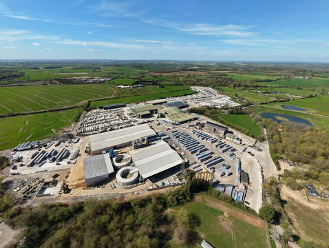 Aerial view of a concrete product supplier facility with industrial warehouses and storage yards surrounded by green fields in Ellistown, England, United Kingdom.