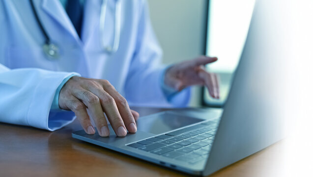 Close-up of doctor working on laptop in medical office. Concept of healthcare technology, telemedicine, online consultation, and digital health services.