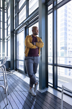 African American man leaning on steel column in atrium looking at city through glass wearing jacket