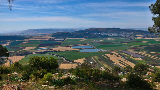 Aerial view of agricultural valley from Mount Tabor in Northern Israel with geometric fields, irrigation reservoirs and rolling hills under soft daylight landscape panorama