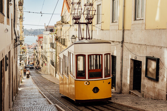 Historic yellow tram on steep Lisboa street in warm photography style on sunny urban backdrop, concept of travel and culture