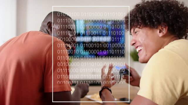 Two men gaming at table, right man using controller causing binary overlay, fading, laughing