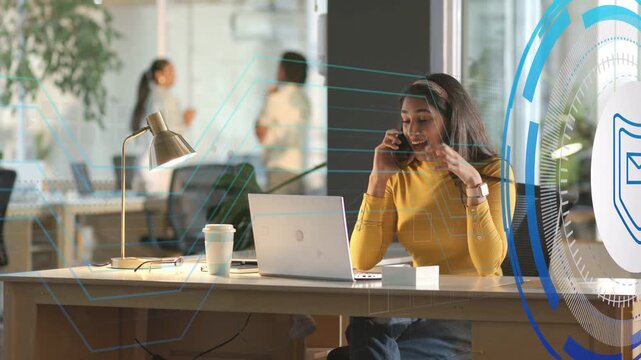 Woman speaking on smartphone, glancing at laptop and causing animated security HUD protecting email