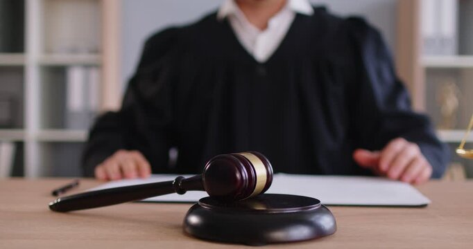 Closeup cropped video of man judge knocking gavel having court verdict sitting at the desk on workplace in courtroom. Male justice worker working indoors. Legal law and justice concept. 4k video.
