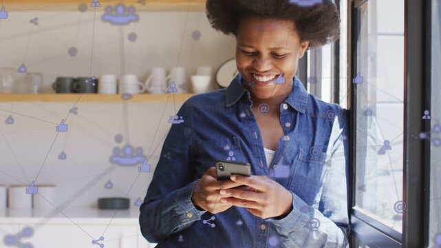 Woman tapping smartphone by window, causing animated social icons drifting while reading messages