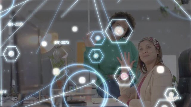 Two coworkers raising hands at desk, controlling hexagon grid overlay for technology demo