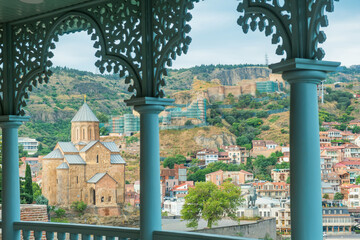 View of Tbilisi old town with Metekhi Church framed by decorative wooden balcony arches and cityscape. Georgian landmark combining architecture, culture and urban landscape. Travel destination © samael334