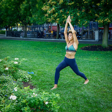 Athletic woman practicing yoga warrior pose in garden in New York City