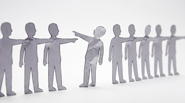 Row of paper cutout figures pointing fingers at a single crumpled figure, illustrating blame, judgment, scapegoating, social exclusion and peer pressure