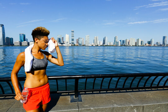 Athletic woman wiping sweat with towel after outdoor workout by waterfront in New York City