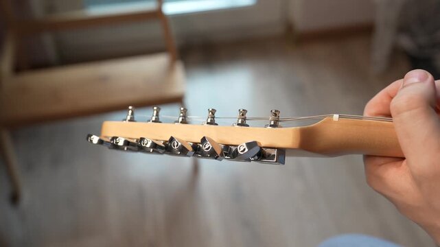 A man Tuning his guitar and playing it. Top lock tuners on double cut electrical guitar.