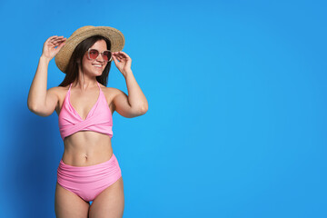 Woman in pink swimsuit, hat and sunglasses on light blue background. Space for text