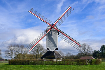 Fototapeta premium Windmill De Leystermolen (Mol, Belgium) in a rural landscape with green grass and cloudy sky, combining classical architecture and functionality.