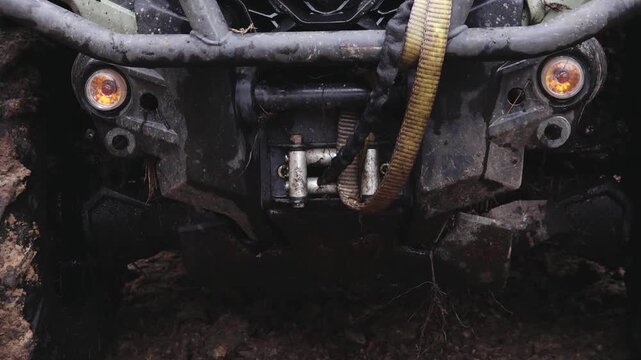 Six-wheeled ATV front view with visible winch and lights, showcasing rugged design and muddy terrain in outdoor environment