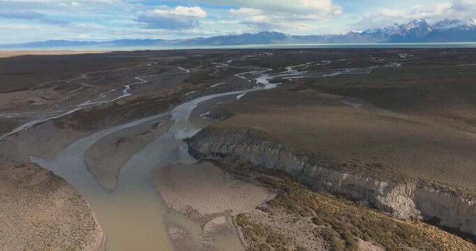 4K video; slow backward drone flight over a braiding muddy river on the pampas of Patagonia with Lago Viedma and the snow covered mountains of the Andes in the background, southern Argentina