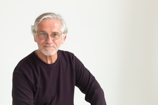 Older man with glasses sitting against white background