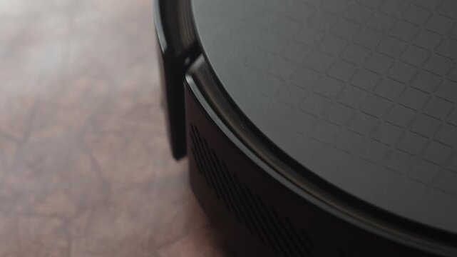 Close-up of a male finger pressing the start button on a black robot vacuum cleaner. The smart device begins to rotate and activates for home cleaning