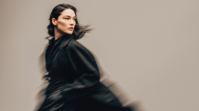Stylish woman in motion blur running in dark coat against beige background with copy space, modern fashion portrait for dynamic advertising design