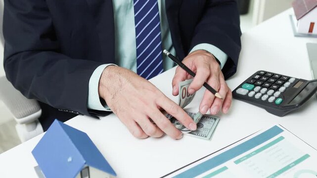 
Businessman shields tiny house with hand. Office desk holds coffee cup and pens. Professional demeanor suggests protection or security. Ideal for insurance, real estate, or financial services