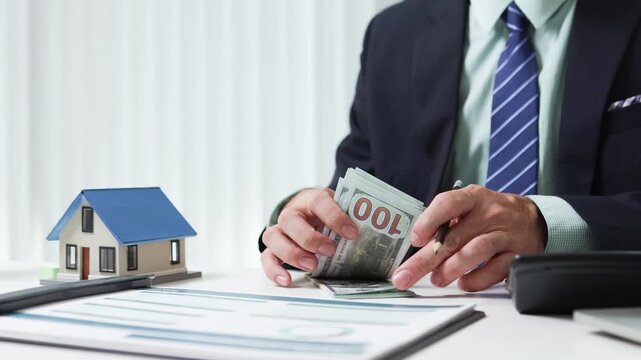 
Businessman shields tiny house with hand. Office desk holds coffee cup and pens. Professional demeanor suggests protection or security. Ideal for insurance, real estate, or financial services