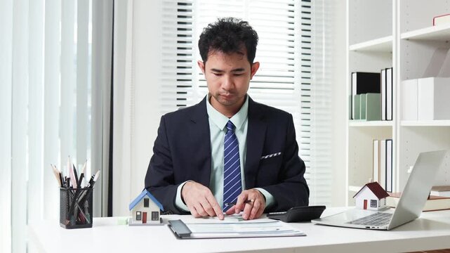 
Businessman shields tiny house with hand. Office desk holds coffee cup and pens. Professional demeanor suggests protection or security. Ideal for insurance, real estate, or financial services