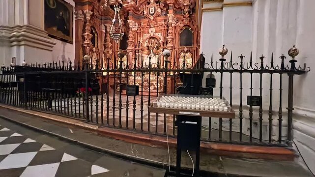 A visitor inserts a coin to light digital votive candles inside the historic Granada Cathedral, featuring a checkered marble floor and a golden Baroque altar in the background.