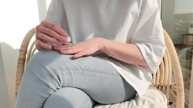 Woman applies oil on cuticle finishing manicure routine at home. Female moisturizes skin around nails with care. Beauty concept highlights hygiene and selfcare for healthy fingernails