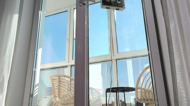 Hand presses remote activating robot cleaner on window glass during sunny day. Device starts washing surface using automated control system. Spring cleaning routine concept for modern home
