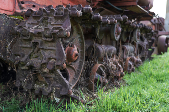 Rusty tractor track detail in grass, weathered crawler machinery texture for agriculture, industrial decay, mechanical engineering, vintage equipment.