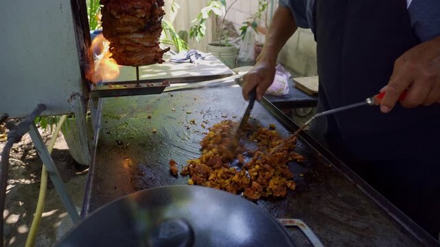 Taquero cooking tacos al pastor on hot griddle