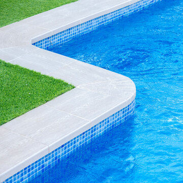 Close-up of a luxury swimming pool edge with blue water, mosaic tiles, and green grass, showcasing a modern outdoor design and relaxing summer atmosphere - relaxation and luxury lifestyle concept