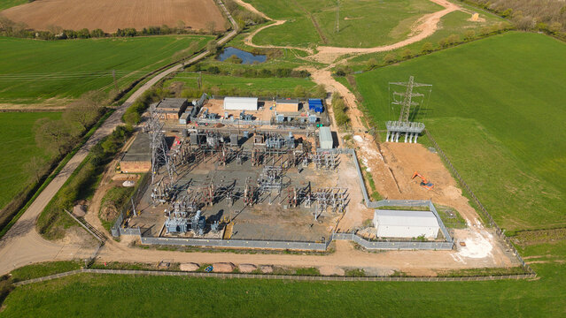 Aerial view of Coalville Substation with electrical transformers, power pylons, and an orange excavator surrounded by green fields in Coalville, England, United Kingdom.